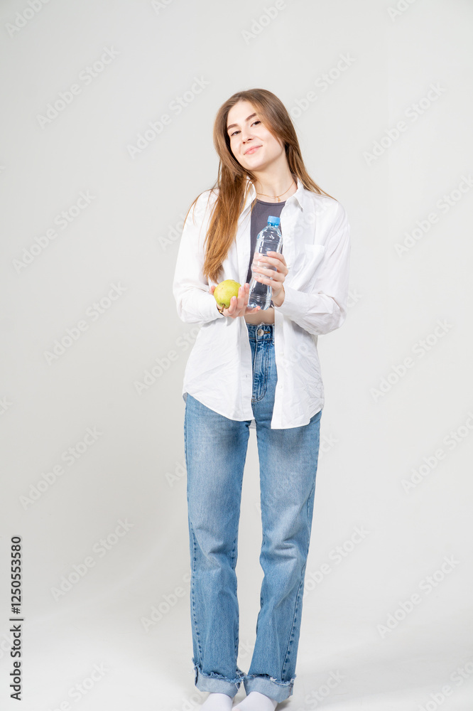 Attractive young girl in white shirt and jeans with bottle of water and apple posing on white background