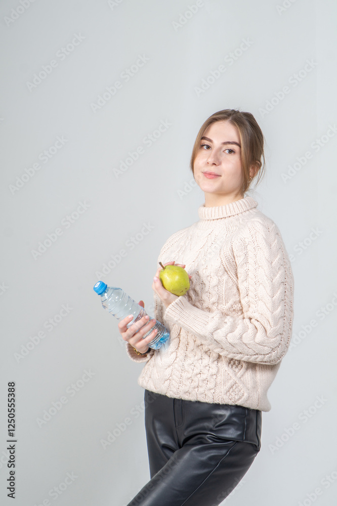 Attractive positive young girl in beige sweater with bottle of water posing standing on white background Attractive positive young girl in beige sweater with bottle of water posing standing on white background