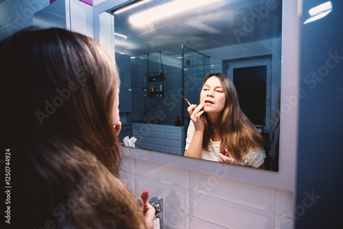 A woman stands in front of a mirror. In her hands is red lipstick. She is obviously preparing for a date. photo
