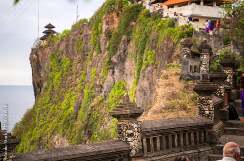 Obraz na płótnie Ancient stone pathway with ornate pillars stretches along Uluwatu's cliff face, leading to temple structures crowned with traditional multi-tiered pagodas against ocean backdrop w salonie