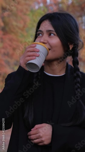 Stylish and relaxed, she sips her hot coffee cup, finding joy and peace outdoors.