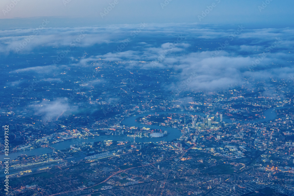 Aerial view of London through early morning clouds with Thames river flowing at golden hour sunrise