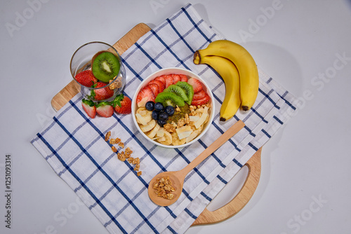 A vibrant and healthy smoothie bowl topped with fresh strawberries, blueberries, kiwi, banana slices, almonds, and pistachio. Placed on a paper cup.