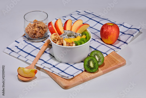 A delicious and nutritious granola bowl topped with fresh apple, kiwi, banana slices, coconut flakes, and almonds. Placed on a wooden board with a checkered napkin.