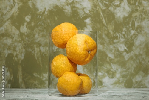 Obraz na plátně In an artistic display, several fresh yuzu lemons gather in a transparent vase a