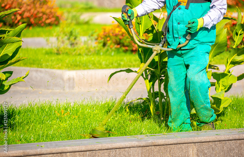 A worker mows the lawn with a manual lawn mower on the streets of the city. Mowing garden meadow lawn. Summer work in the garden.