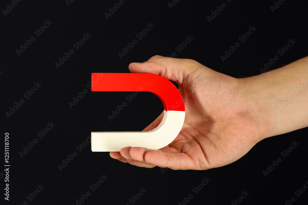 Fototapeta premium Man holding horseshoe magnet on dark background, closeup