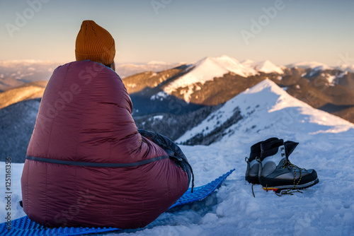 Φωτογραφία Young Woman in sleeping bag at winter mountains watching alpenglow sunrise