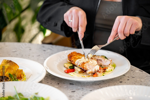 A close-up view of a person cutting a deliciously plated chicken dish with vegetables. A second dish is visible nearby, highlighting an elegant dining experience. photo