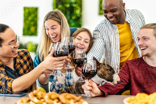 Photography Young multiethnic people with dog drinking and toasting red wine at lunch party