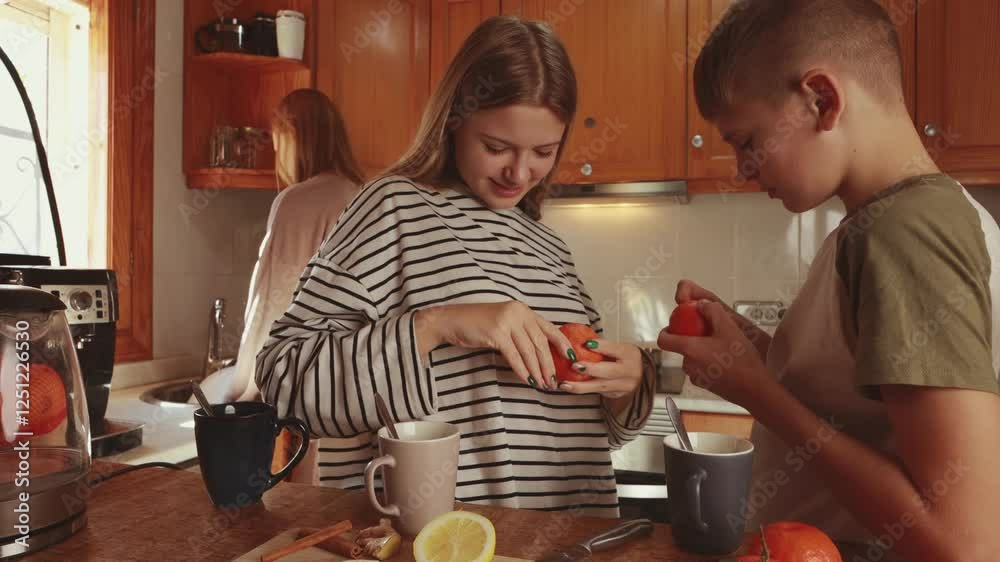 Siblings enjoy peeling mandarins together in a cozy kitchen, their mother washing dishes in the background, creating a heartwarming scene of family togetherness