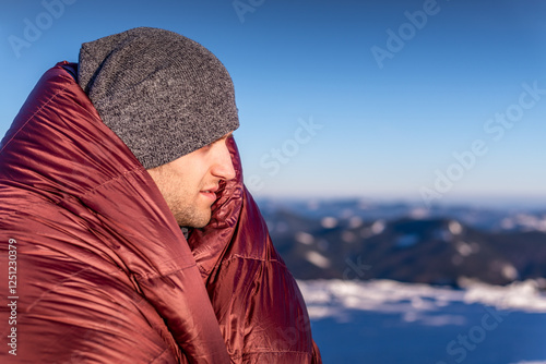 Portraite of young Man Wrapped In A Warm Sleeping Bag Standing On The Background Of Snowy Mountain Peaks. First Morning Light photo