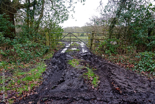 A muddy field entrance with puddles after heavy rain