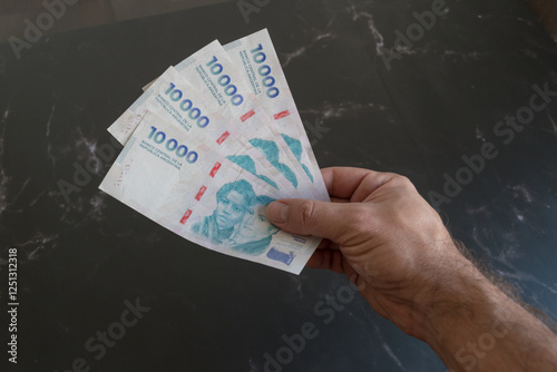 billetes de 10 mil pesos argentinos sostenidos por la mano de un hombre latino. photo