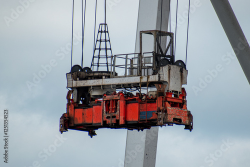 A detailed view of a spreader on a large dockside crane, framed against a backdrop of blue, cloudy skies.
