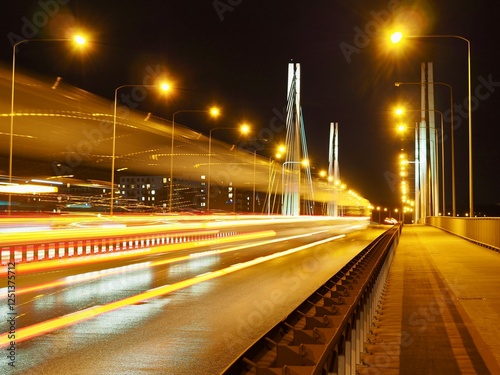 A striking long exposure captures vibrant light trails on a modern bridge, highlighting urban movement and architectural design against a night sky backdrop