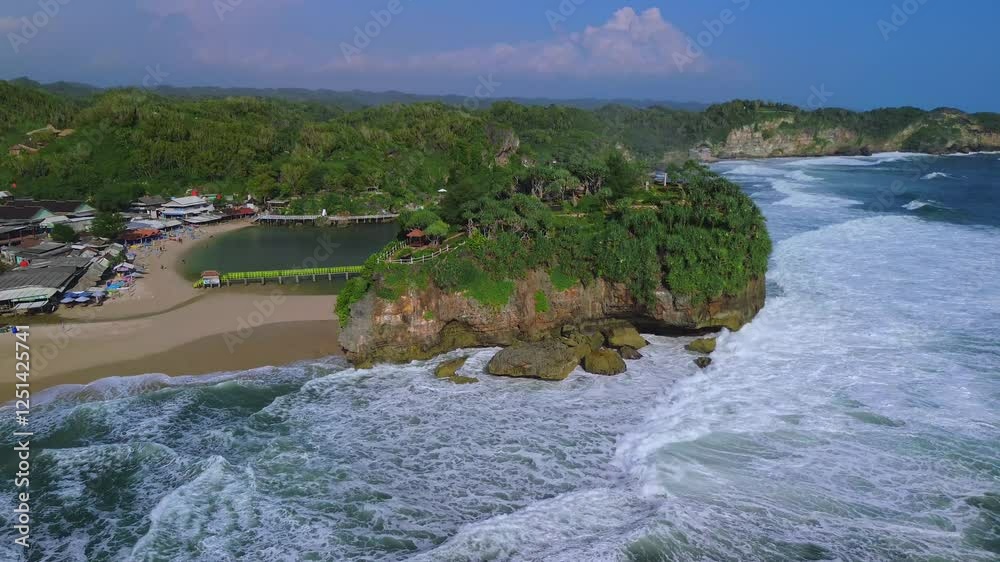 Drone view of white sandy beaches, coral rocks, hills with trees, big waves from the ocean and rip currents which are also a tourist destination known as Drini Beach Gunung Kidul Yogyakarta Drone view of white sandy beaches, coral rocks, hills with trees, big waves from the ocean and rip currents which are also a tourist destination known as Drini Beach Gunung Kidul Yogyakarta