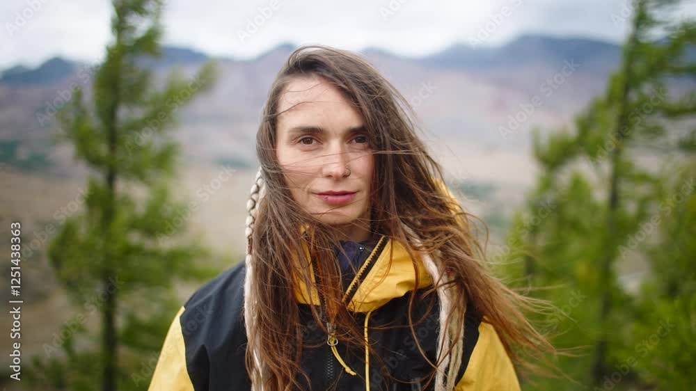 Young woman hiker with dreadlocks, wearing a vibrant yellow jacket, embracing the wind and feeling the freedom of the mountains, surrounded by lush trees in the background Young woman hiker with dreadlocks, wearing a vibrant yellow jacket, embracing the wind and feeling the freedom of the mountains, surrounded by lush trees in the background