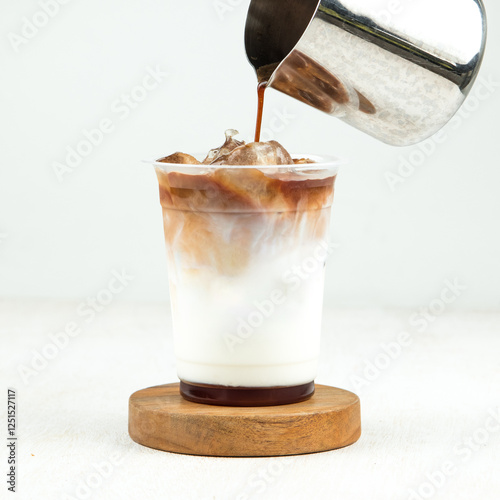 Creamy layers of iced coffee and milk are created as rich brown syrup is poured into a clear cup resting on a wooden coaster