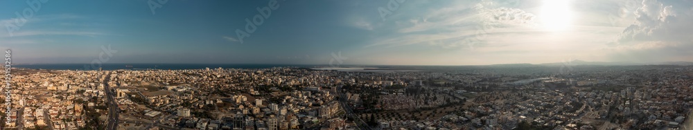 Aerial panoramic view of a sprawling cityscape under a partly cloudy sky. Aerial panoramic view of a sprawling cityscape under a partly cloudy sky.