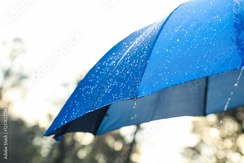 Open blue umbrella under pouring rain outdoors, closeup