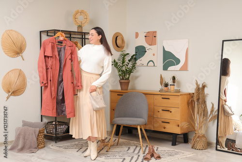 Young woman with stylish coat near clothes rack at home