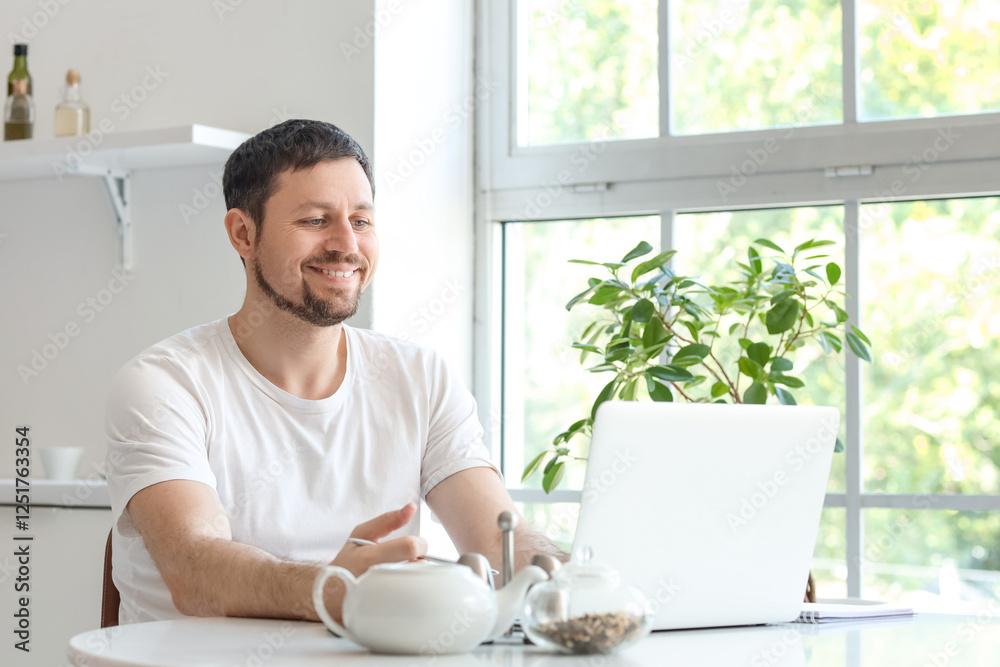 Young male teacher with laptop and notebook giving online lesson at home