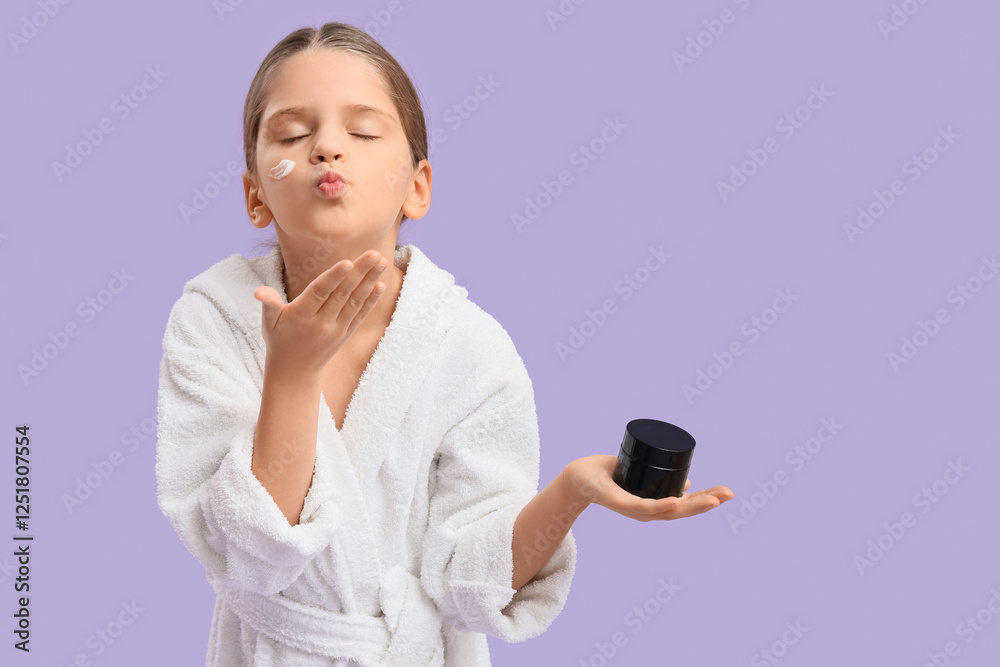 Cute little happy girl in bathrobe with jar of cream blowing kiss on purple background Cute little happy girl in bathrobe with jar of cream blowing kiss on purple background