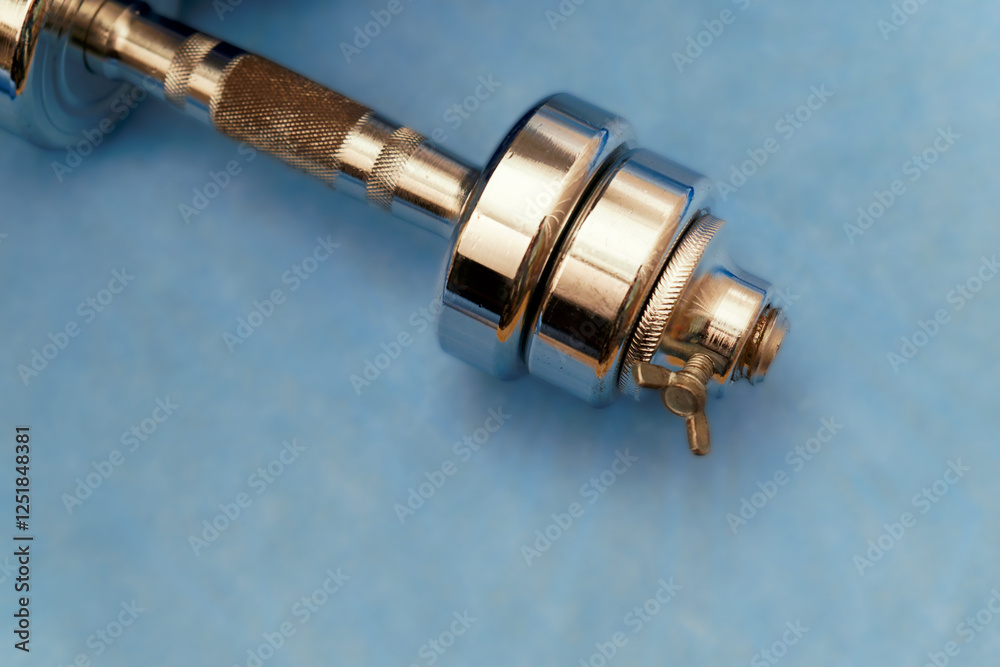 Shiny metal dumbbell resting on blue surface