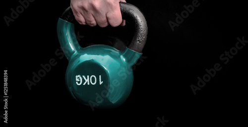 Hand firmly gripping a heavy kettlebell on black photo