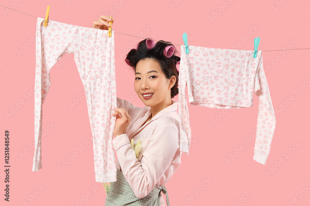 Happy young Asian woman with hanging laundry and clothespins on pink background Happy young Asian woman with hanging laundry and clothespins on pink background
