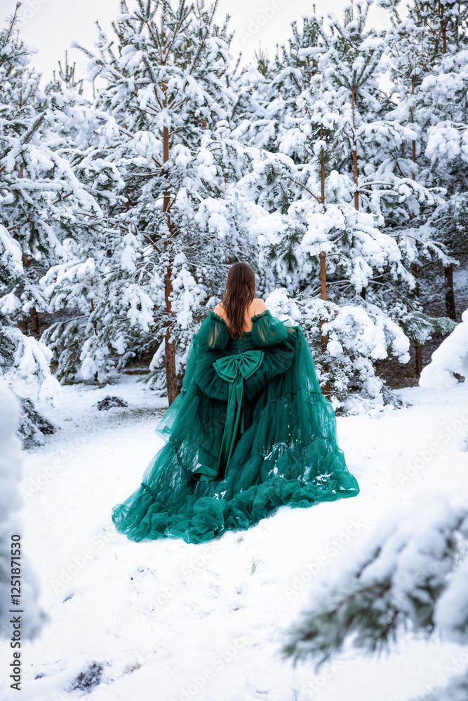A woman in a flowing green dress stands with her back turned in a snow covered forest. Tall pine trees frame the winter landscape, creating contrast. A woman in a flowing green dress stands with her back turned in a snow covered forest. Tall pine trees frame the winter landscape, creating contrast.