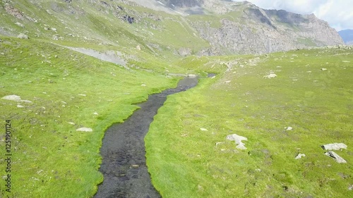 a serene and natural scene featuring a winding stream flowing through a valley in Queyras, France