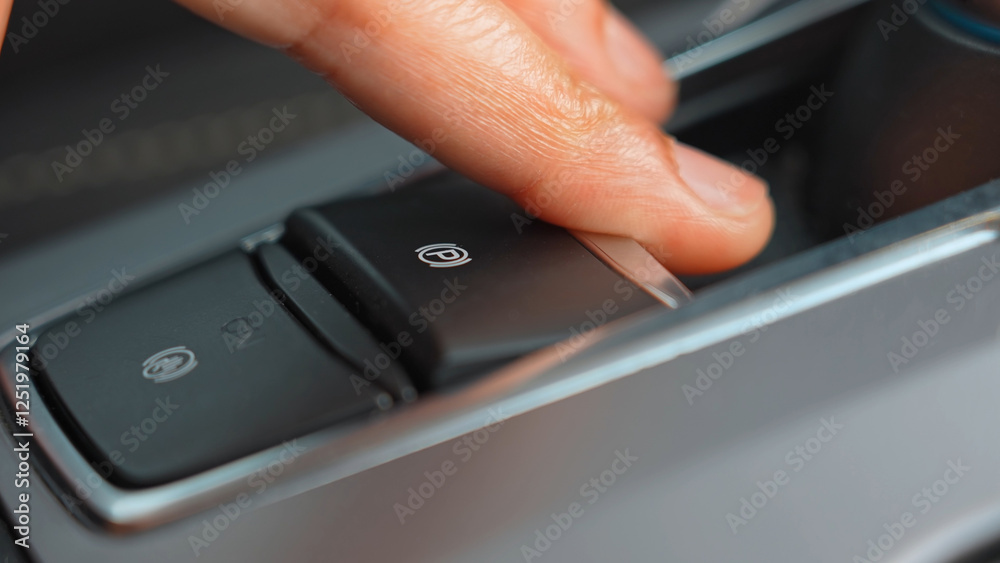 Woman's fingers activate the hand brake in the car. Close-up view in the vehicle, finger pressing the electric parking brake. Driving modern car. Woman's fingers activate the hand brake in the car. Close-up view in the vehicle, finger pressing the electric parking brake. Driving modern car.