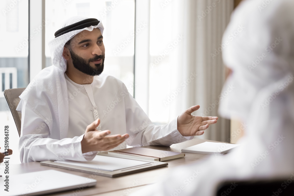 Young Arabic businessman in traditional kandora and ghutra attire engaged in conversation, discussing strategic ideas, partnership opportunities, corporate goals. Business communication, negotiations Young Arabic businessman in traditional kandora and ghutra attire engaged in conversation, discussing strategic ideas, partnership opportunities, corporate goals. Business communication, negotiations