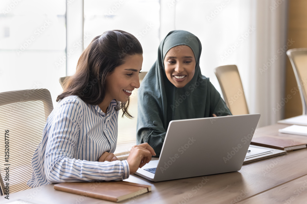 Two multicultural women engaged in collaborative activity on laptop, planning upcoming tasks or scheduling appointments, reviewing project proposal, analyzing data or statistics relevant to their work Two multicultural women engaged in collaborative activity on laptop, planning upcoming tasks or scheduling appointments, reviewing project proposal, analyzing data or statistics relevant to their work