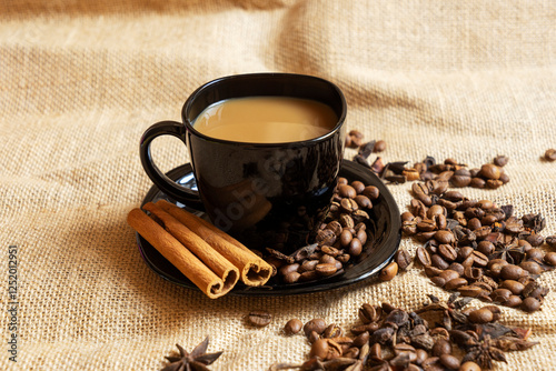 A black cup with a saucer and coffee and coffee beans on a brown cloth background