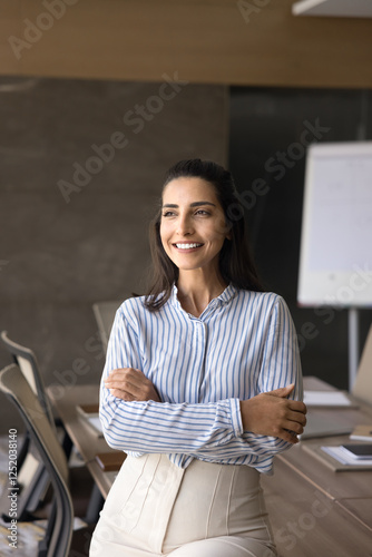 Beautiful competent businesslady posing alone in modern conference room, smiling, looks away, exuding professionalism, feel satisfied with career growth, business achievement, vertical office portrait