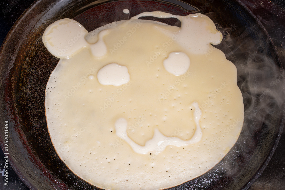 Creative pancake in a pan resembling a bear face, with eyes, nose, and smiling mouth.
