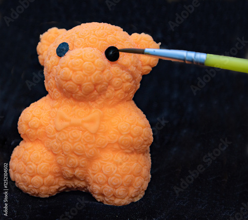 A rubber bear's eye is painted with a brush