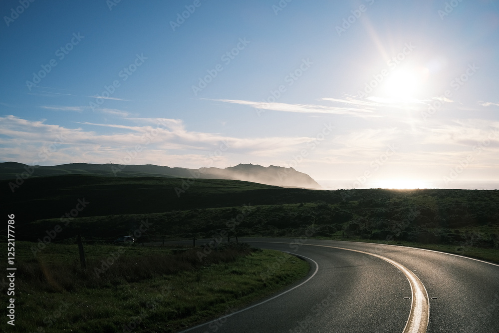 Winding coastal highway through rolling green hills at sunset near Point Reyes, California. Golden light reflecting on the asphalt, mist rising from the Pacific Ocean, dramatic, scenic road trip. Winding coastal highway through rolling green hills at sunset near Point Reyes, California. Golden light reflecting on the asphalt, mist rising from the Pacific Ocean, dramatic, scenic road trip.