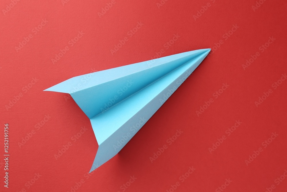 One handmade light blue paper plane on red background, top view One handmade light blue paper plane on red background, top view