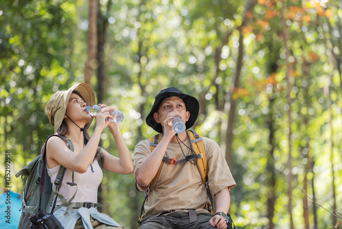 Wallpaper Mural A couple of hikers take a break in the forest, drinking water from bottles to stay hydrated. They wear hats and backpacks, enjoying nature and ensuring hydration during their outdoor adventure Torontodigital.ca