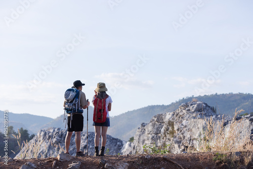 A couple stands together at the edge of a mountain, gazing at the breathtaking landscape ahead. 