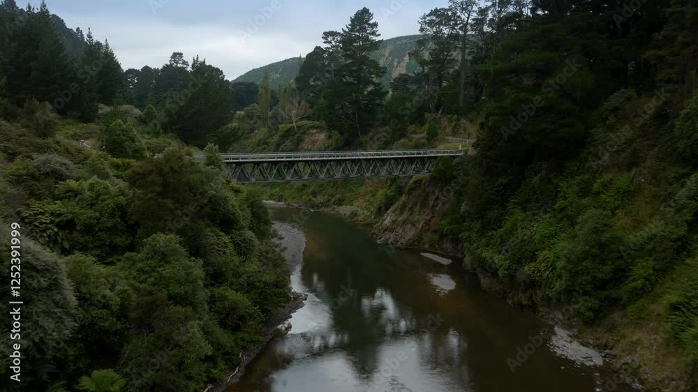 Tranquil river valley with a metal bridge spanning the waterway. Lush green forest surrounds the river. Peaceful natural scene. Ngaruroro River, Kaweka Forest Park, Hawkes Bay, New Zealand Tranquil river valley with a metal bridge spanning the waterway. Lush green forest surrounds the river. Peaceful natural scene. Ngaruroro River, Kaweka Forest Park, Hawkes Bay, New Zealand