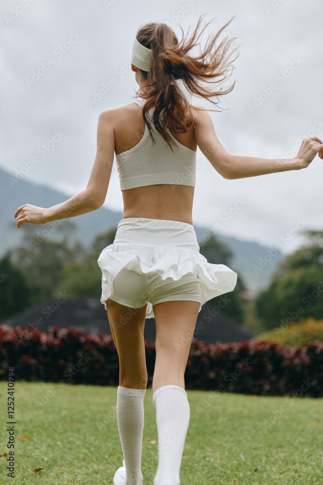 Young athletic model in white sportswear, enjoying an active outdoor lifestyle with flowing hair against a lush green background, conveying a sense of freedom and vitality Young athletic model in white sportswear, enjoying an active outdoor lifestyle with flowing hair against a lush green background, conveying a sense of freedom and vitality