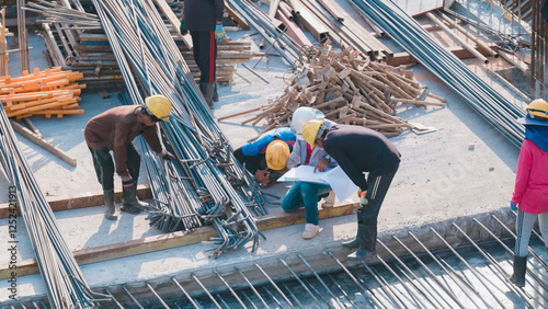 Construction Workers Collaborating on Site, Group of construction workers discusses blueprints and coordinates tasks among steel reinforcements, teamwork and planning in building project