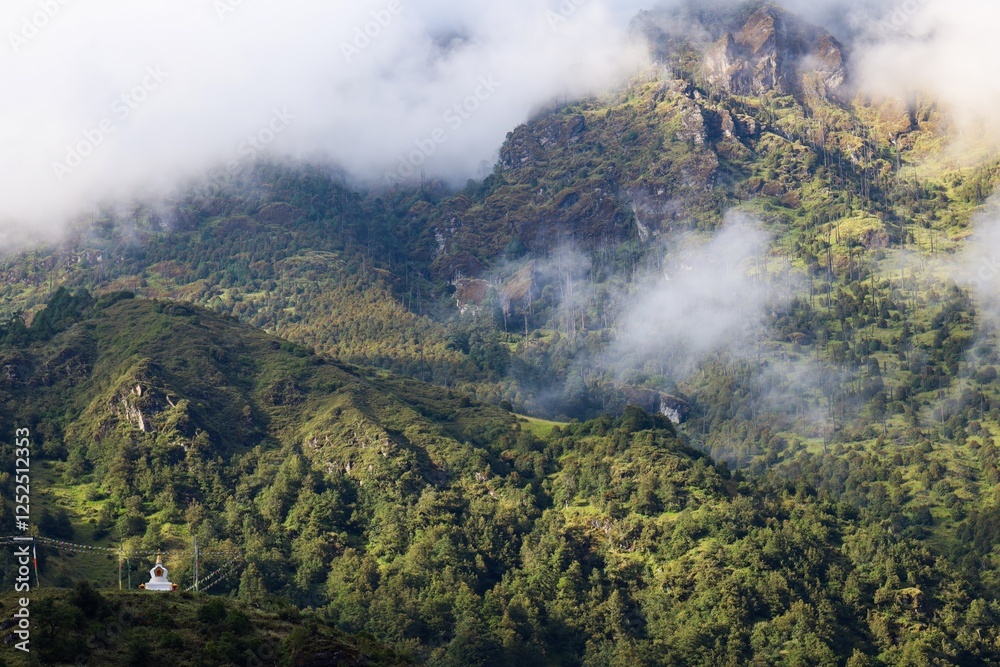 Fototapeta premium Scenic view of lush green hills and misty mountains with a small Tibetan stupa in Gyabla, Nepal, along the trail to Kanchenjunga Base Camp in the majestic Himalayas.