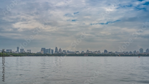 Beautiful calm lake. Ripples on the surface of the water. In the distance, there is green vegetation on the shore. Tall city buildings, skyscrapers against a blue sky and clouds. China. Hangzhou.  photo