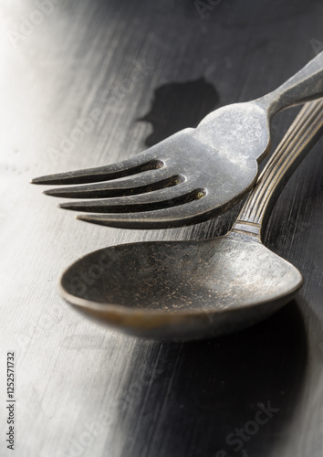 Obraz na płótnie The morning sun shines hits on Ancient worn vintage cutlery on the black background. Close up of Crossed black metal spoon and fork, Highlighting its texture and design, Light and shadow, use it as yo w salonie